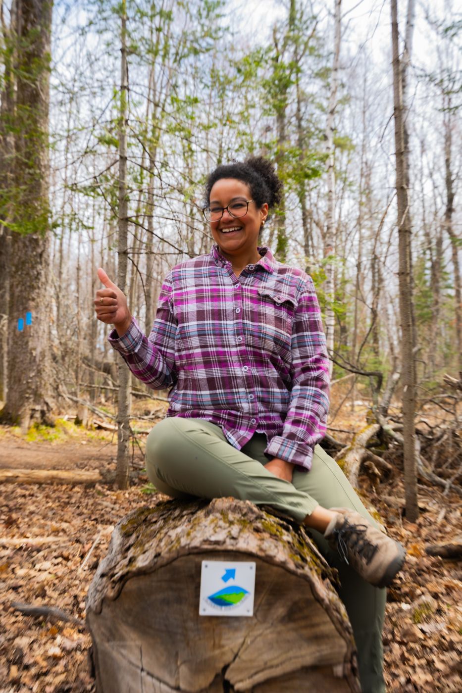 Rachel sitting on a log beside a Superior Hiking Trail marker